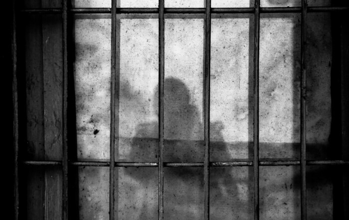 A picture of bars on a jail cell and a shadow of a person on the wall.