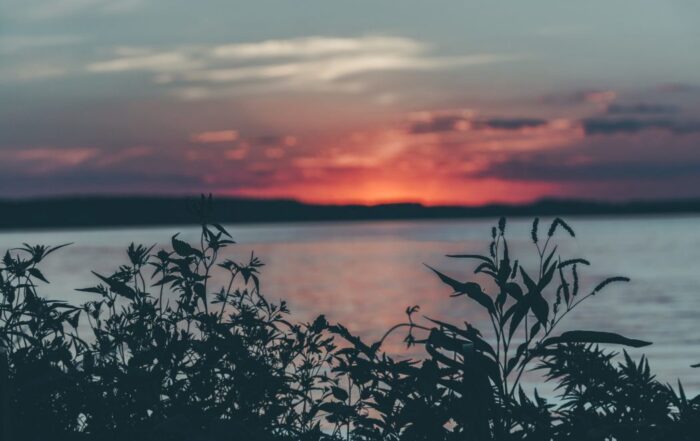 a picture overlooking a body of water with silhouetted hills on the other side and a gorgeous deep pink sunset on the horizon.