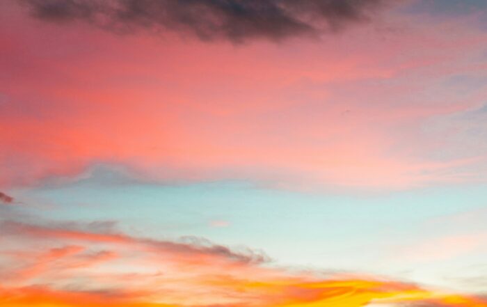 A picture of a beautiful multi-colored sunset with oranges, yellows, pinks, blue, and a dark grey cloud towards the top of the image.