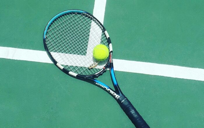 A picture of a tennis racket on the floor of a tennis court with a tennis ball on top of it.