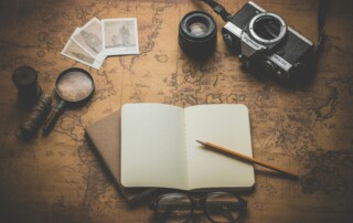 A picture of a notebook open on a map with a spyglass and a film camera and a pair of glasses.