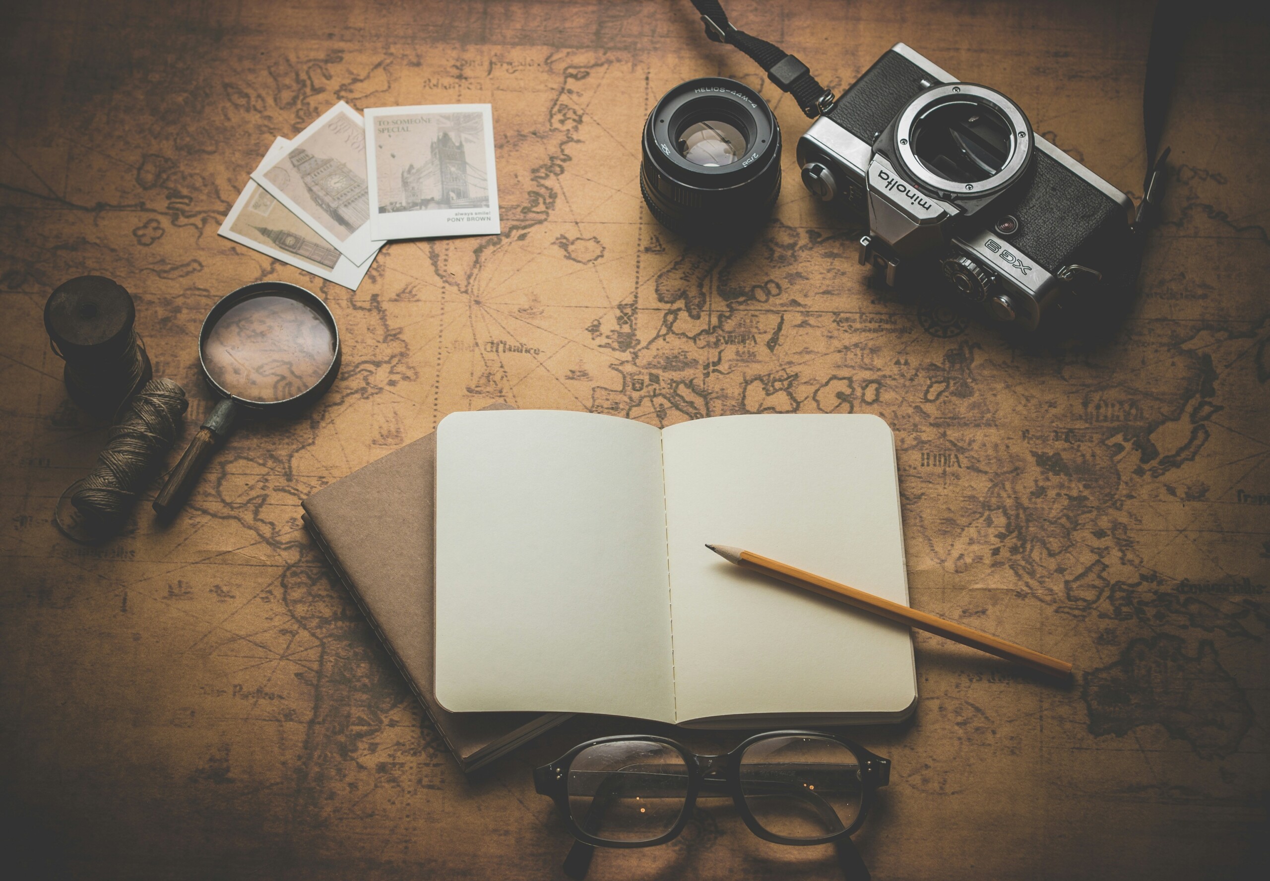 A picture of a notebook open on a map with a spyglass and a film camera and a pair of glasses.