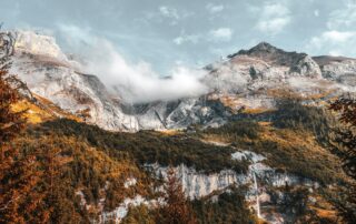 A picture of a large, rugged mountain with greenery on the side of it and blue sky and clouds above.