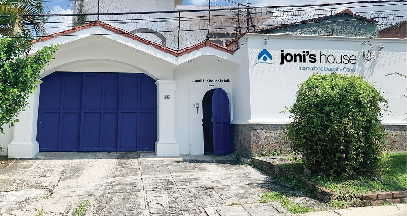 A white building with the Joni’s House logo displayed on the front, with a blue gate and blue door at the entrance