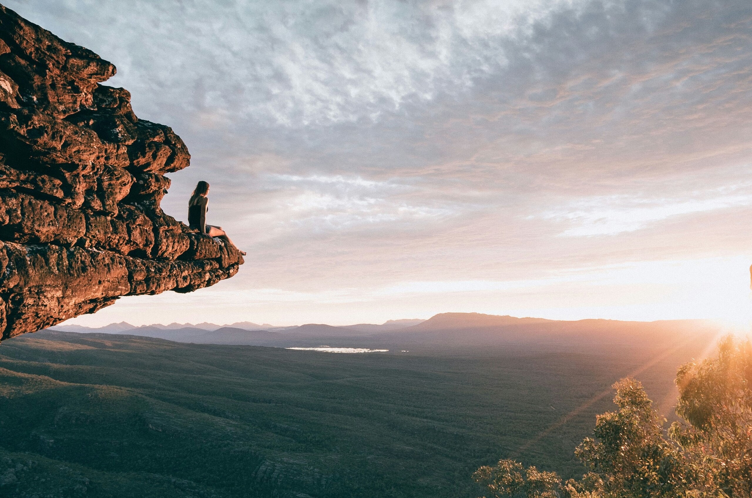 A picture of a woman sitting on a high cliff overlooking a huge valley.