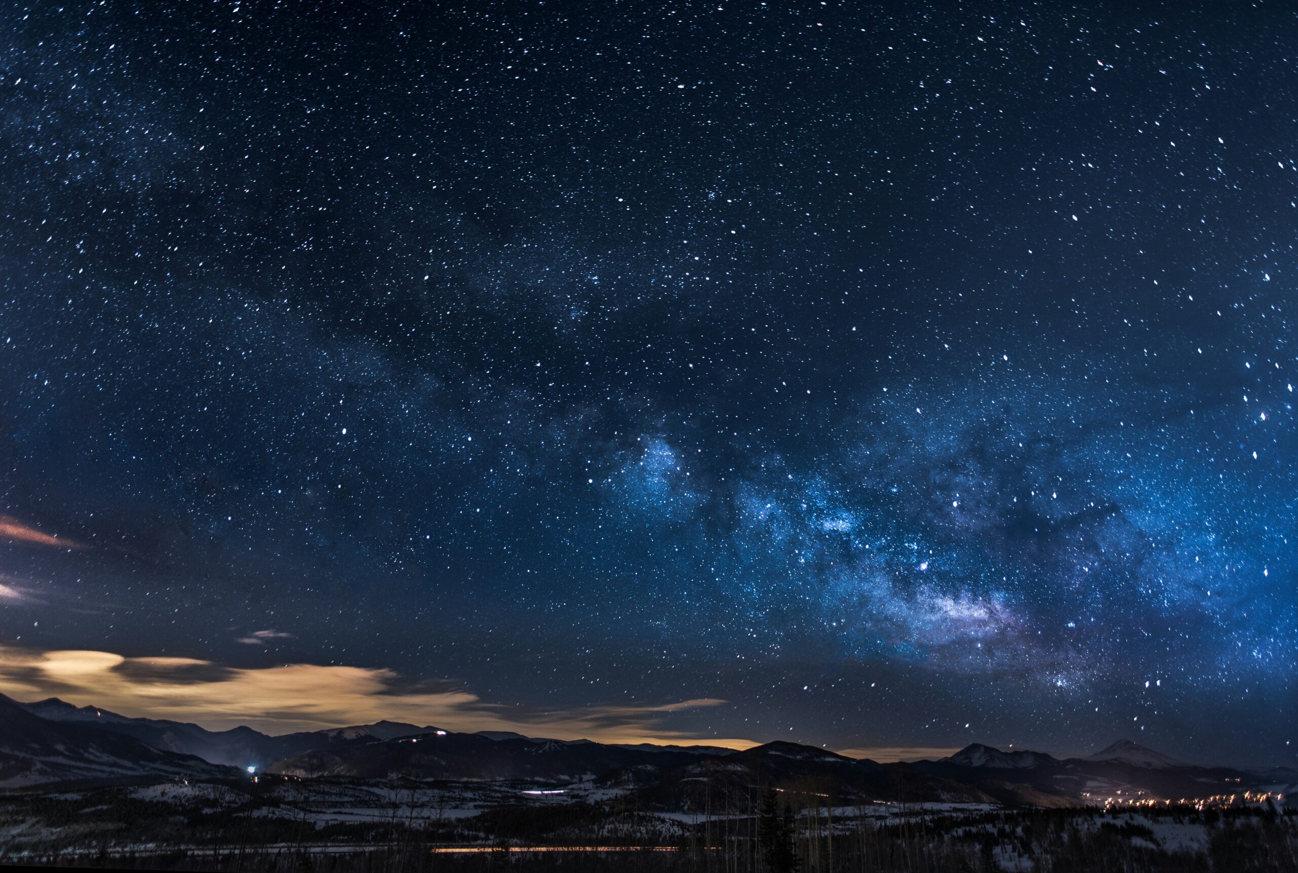 A picture of a starry sky full of thousands of bright stars and visible galaxies. Beneath is a small mountain range with snow at the peaks.