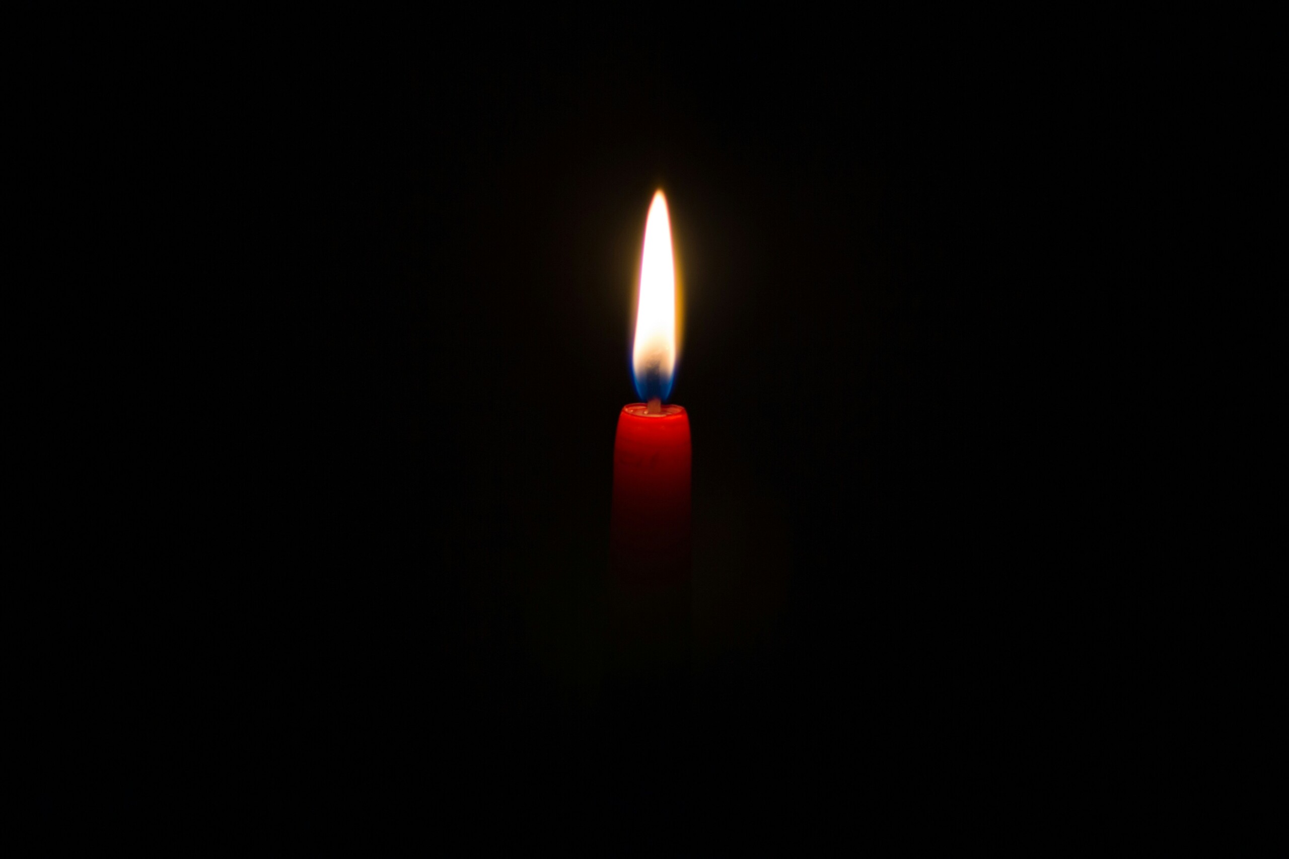 A close-up picture of a candle lit with a dark background behind it.