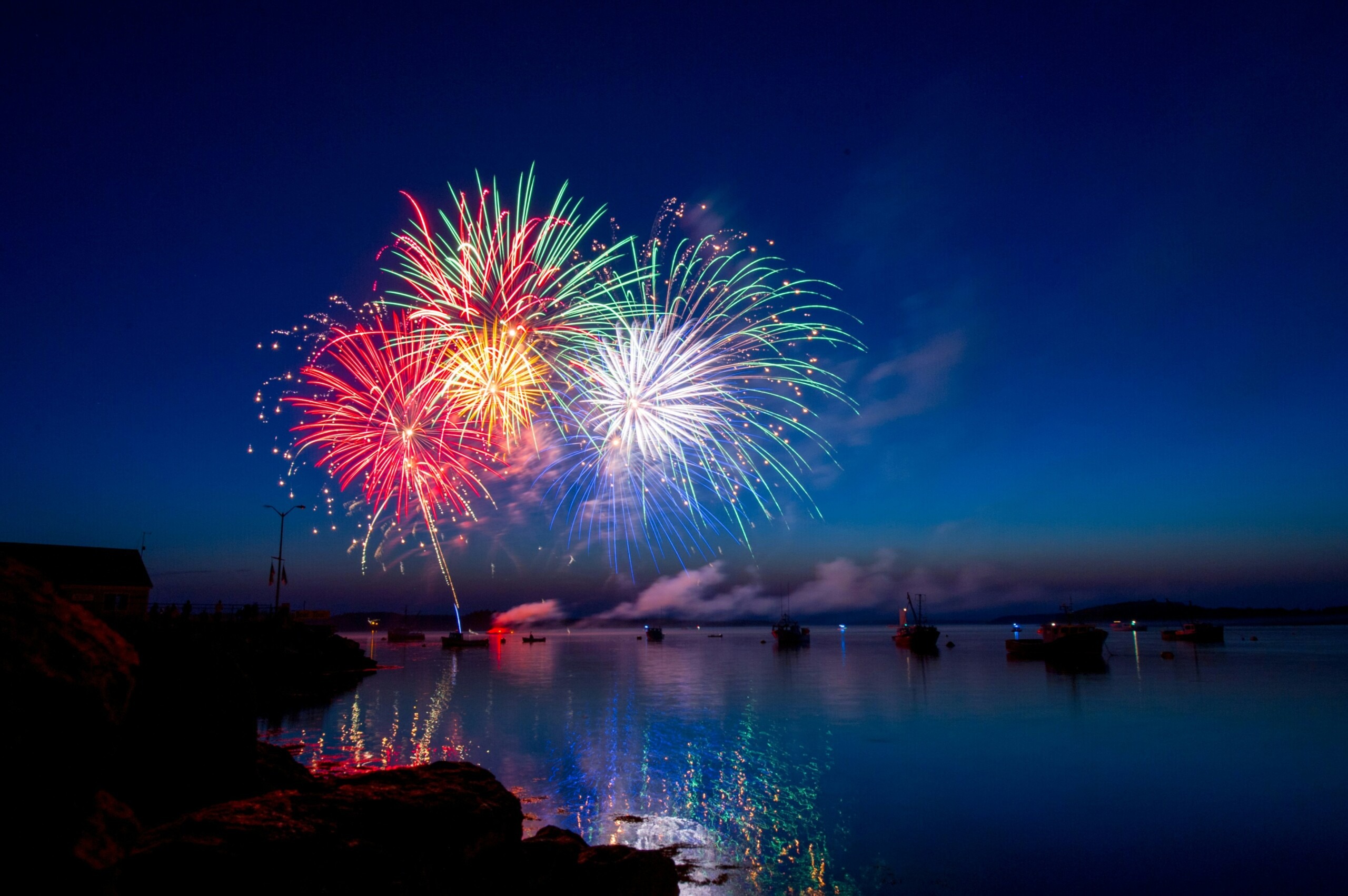 A picture fireworks going off in the dark blue night sky reflecting off the water below.