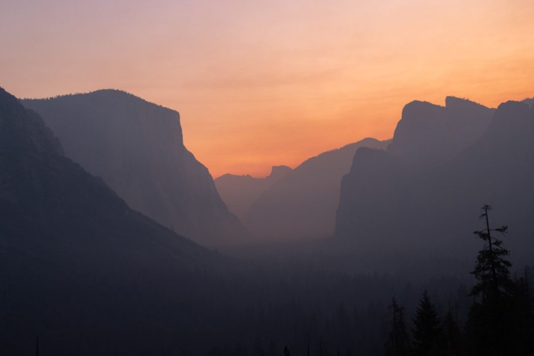 The view from within a valley with tall mountain peaks on either side, a hazy sunset falling over the scene.