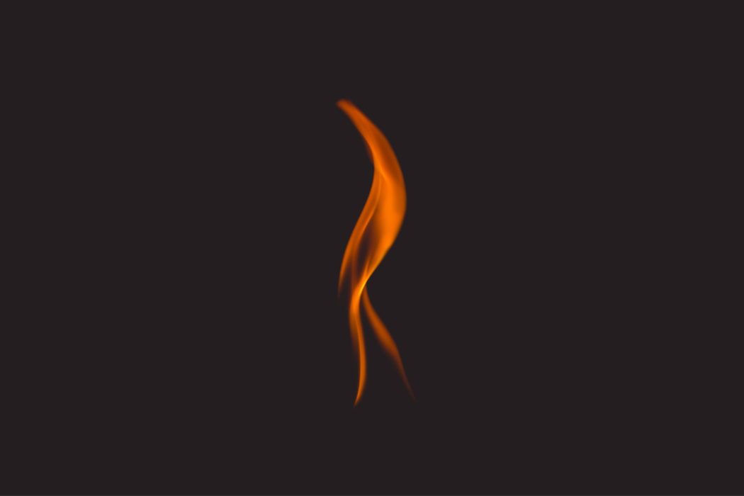 Close up of a single flame of fire against a dark background.