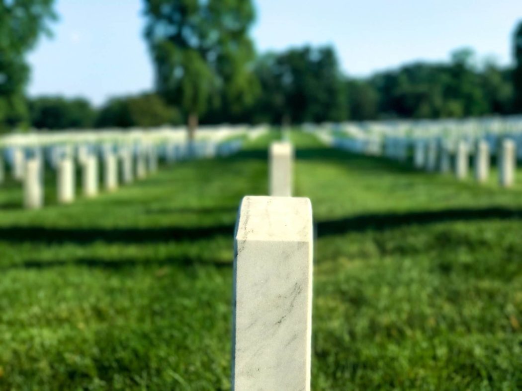 Close up of a tombstone in a long line of other tombstones in a grassy field.