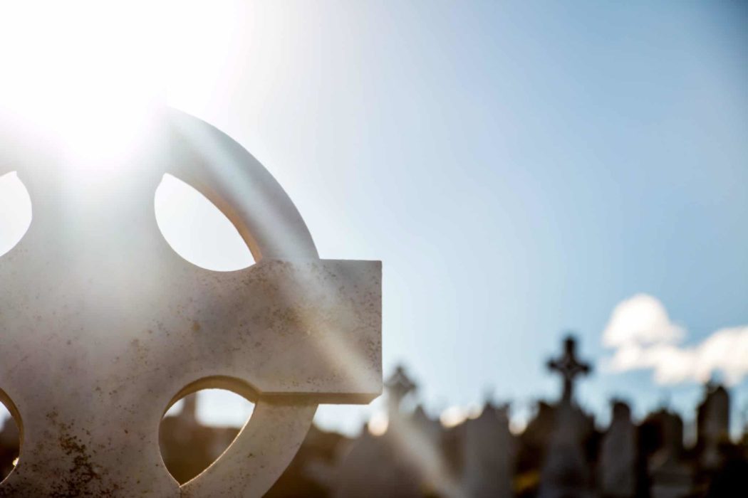 Close up of a gravestone with the sun shining over it and other hazy gravestones in the background.
