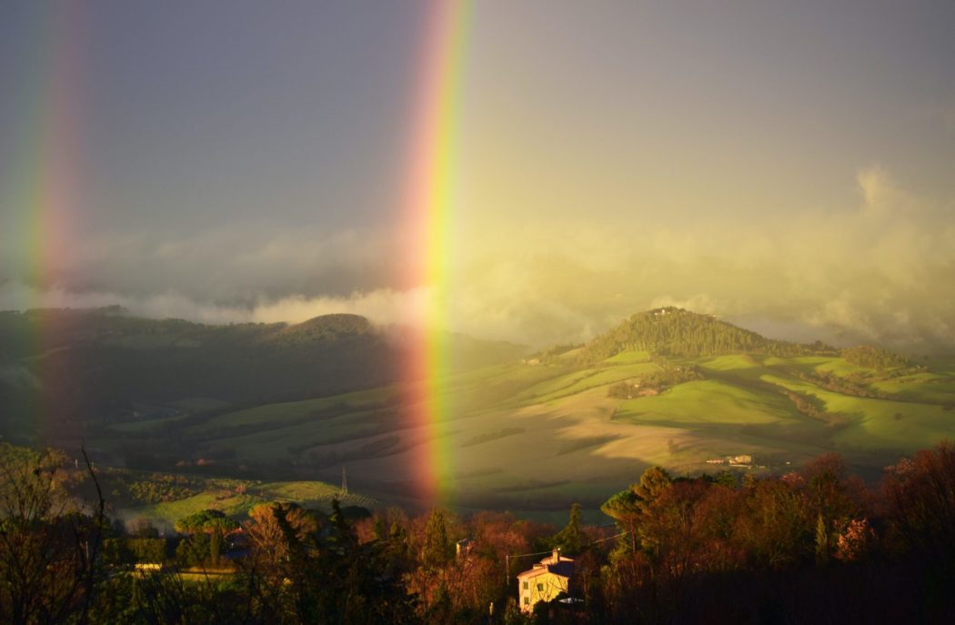 A rainbow coming up over the grassy mountains.