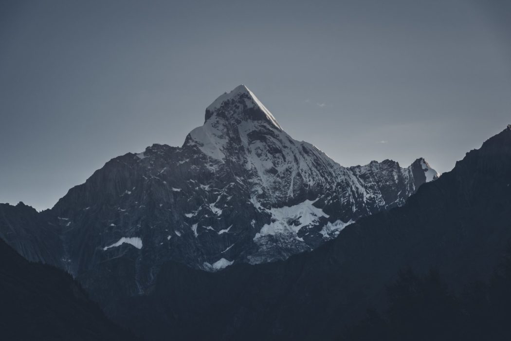 The view from below a rigid mountain peak with snow on top and clear skies above.