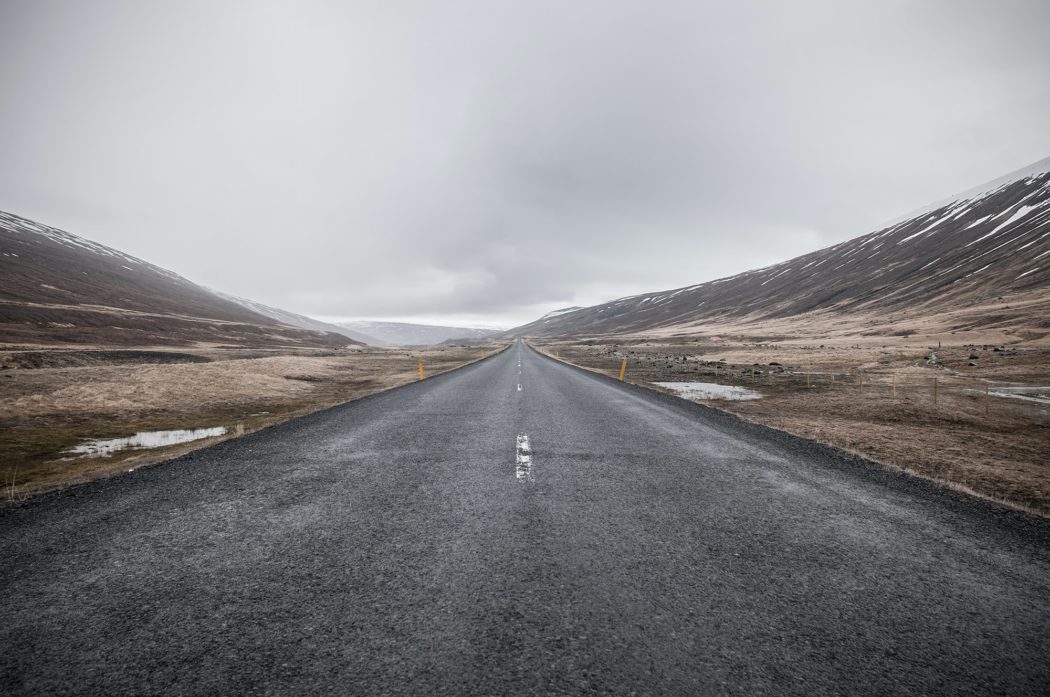 An empty road with hills on either side and clouds above.