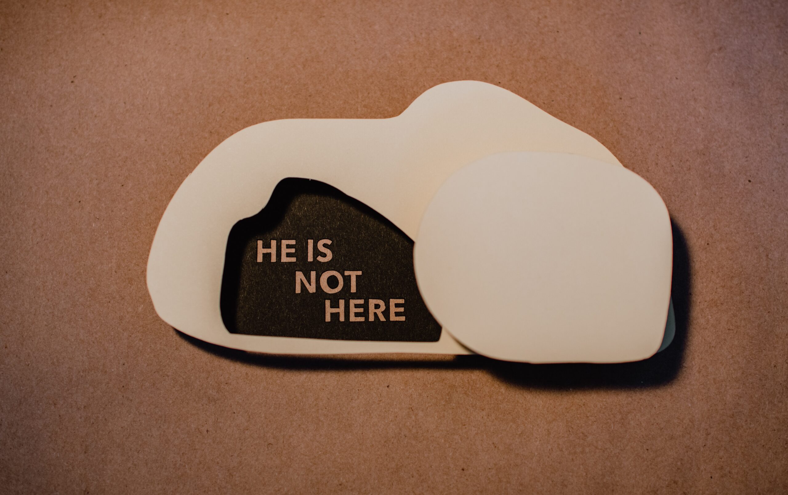 Close up of a small 2-D wooden tomb with the words "He is not here," written inside of the opening.