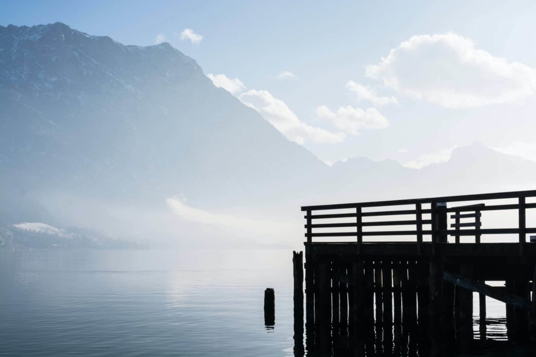 A lake with a wooden dock and mountains surrounding it. 