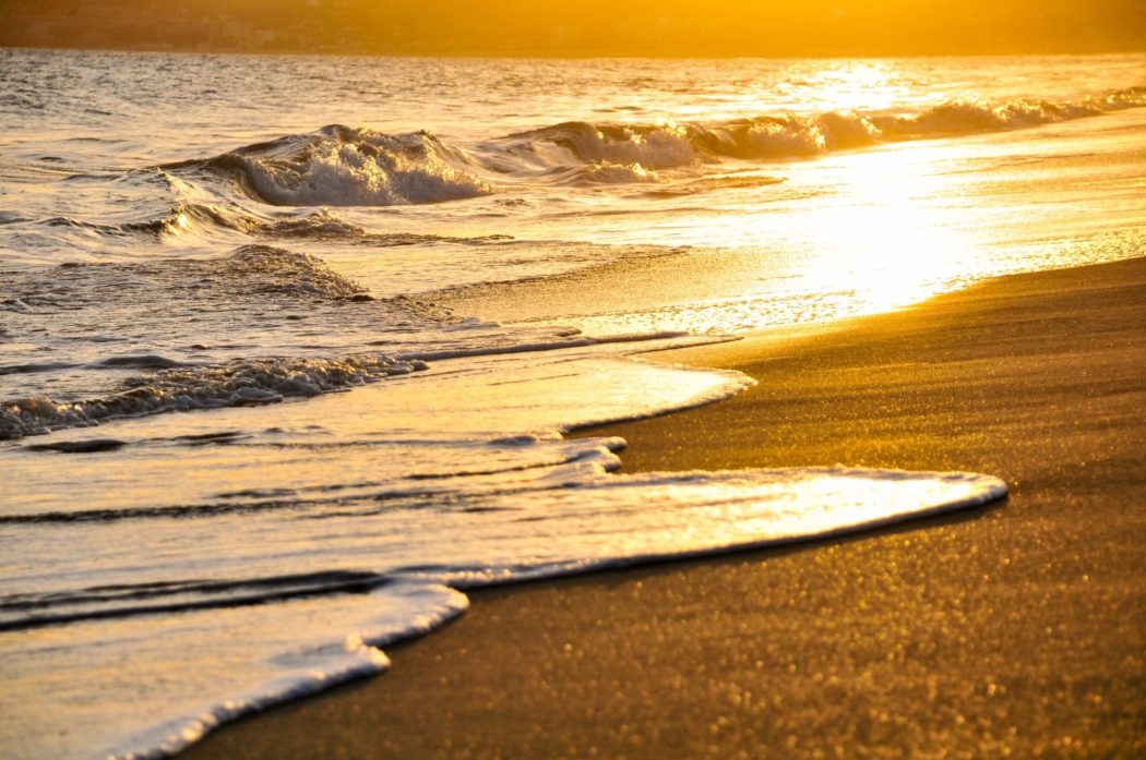Waves crashing on the shore, the sun reflecting off the water.