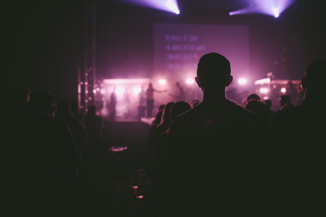 The view from behind a crowd of people facing a stage at a worship service.