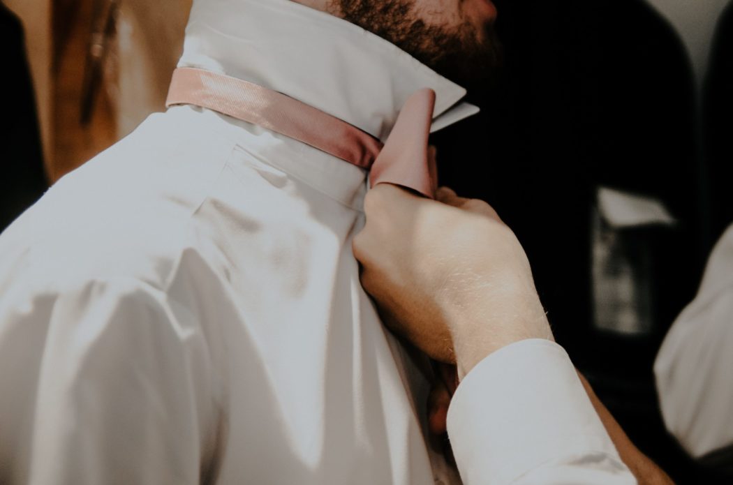 A close-up of a man helping another man adjust his necktie.