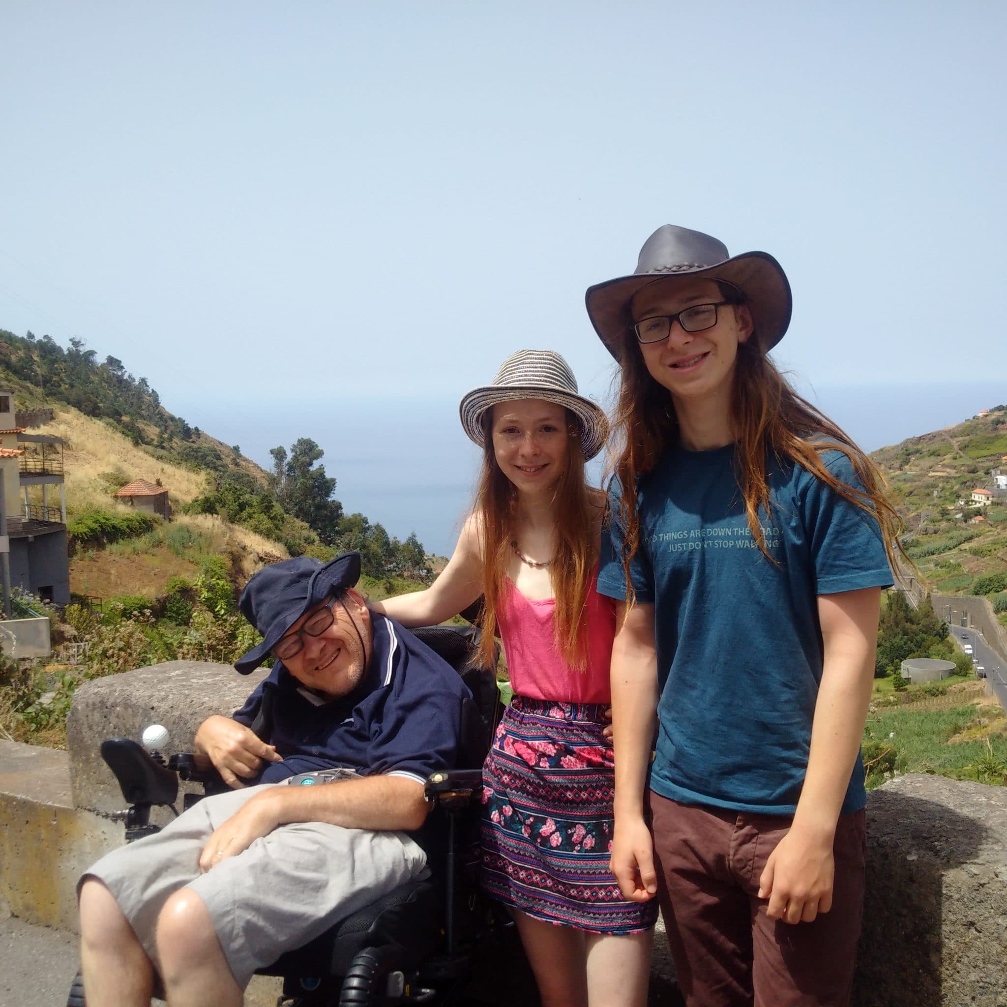 Mountaintop in Spain. Paul Linoewood sits in his wheelchair on the left. In the middle stands Hannah. Standing on the right is Michael.