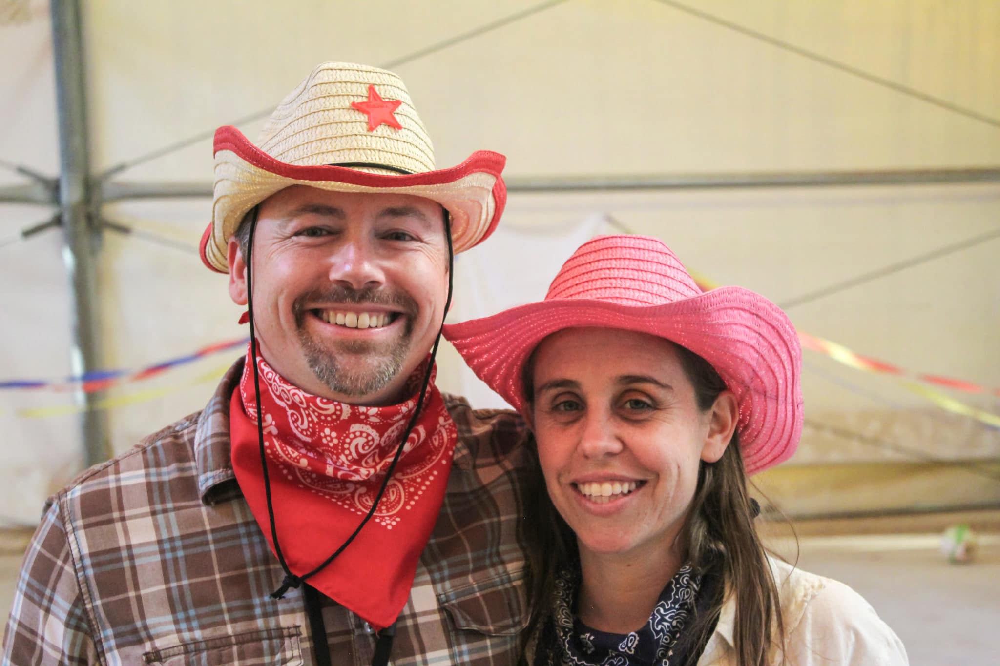 John on the left standing next to his wife Juliana on the right. Both are smiling for the camera while wearing cowboy hats and bandanas around their necks.