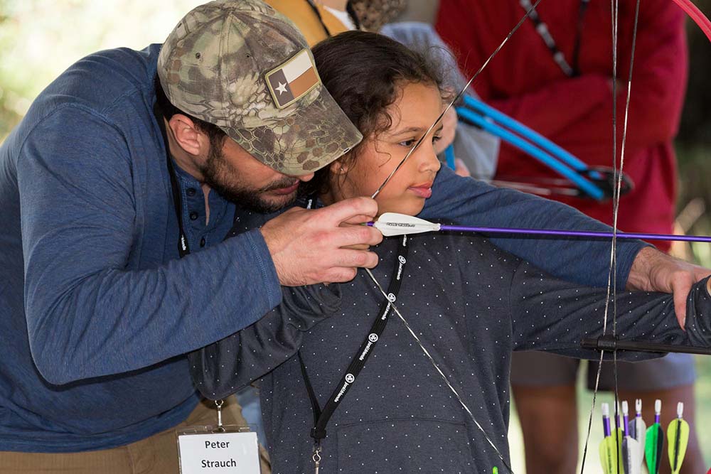 A father teaches his daughter archery at Warrior Getaway