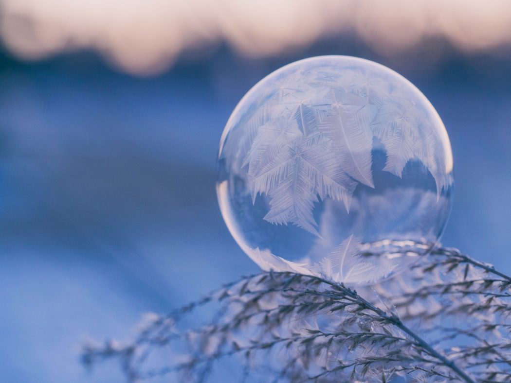 Frozen bubble resting on a plant. Ice crystals have formed on the surface of the bubble, creating intricate patterns that resemble ferns or snowflakes.