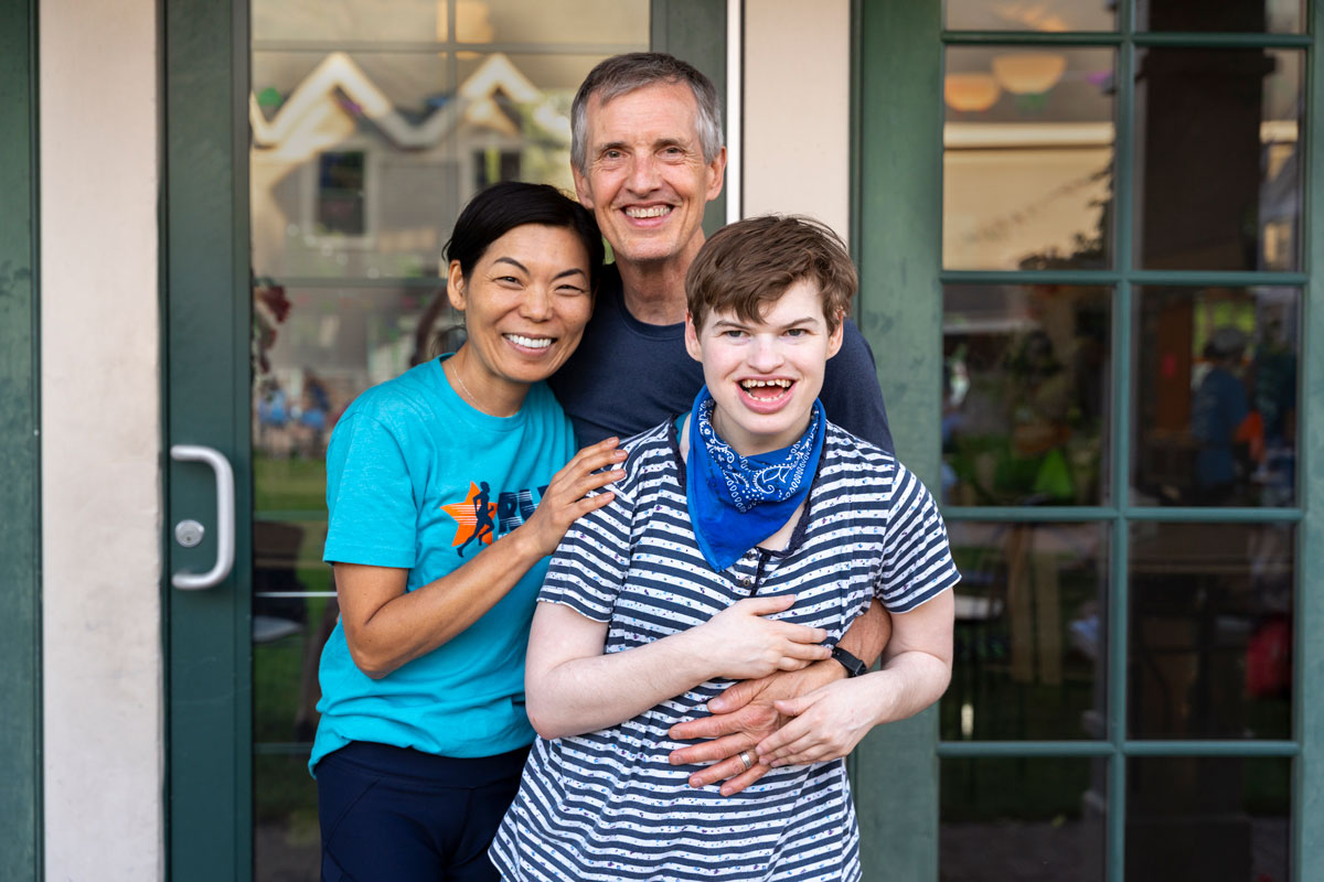 A family photo of a woman and her husband and their daughter with a disability. All are smiling at the camera.