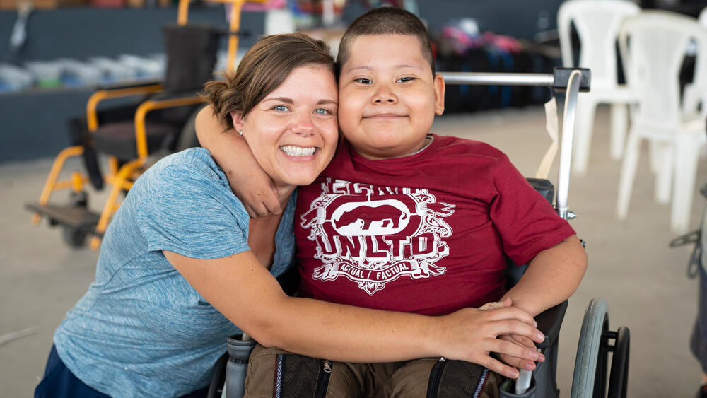 A volunteer embraces a young man in his new wheelchair