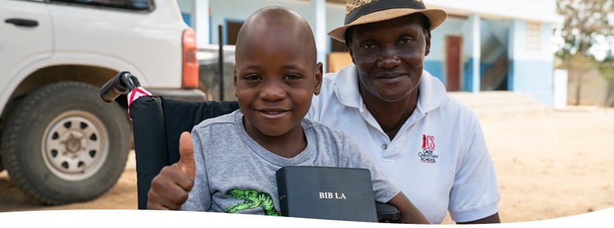 A boy holds his Bible in his new wheelchair as his dad embraces him