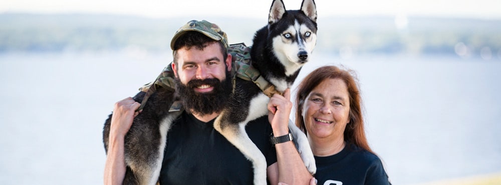 A man with a husky over his shoulders next to a woman smiling at Warrior Getaway