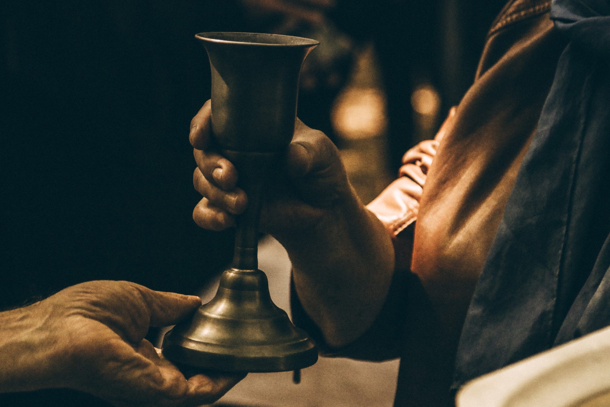 A close-up of a glass cup being handed to another person, who is holding the bottom of the cup with one hand.