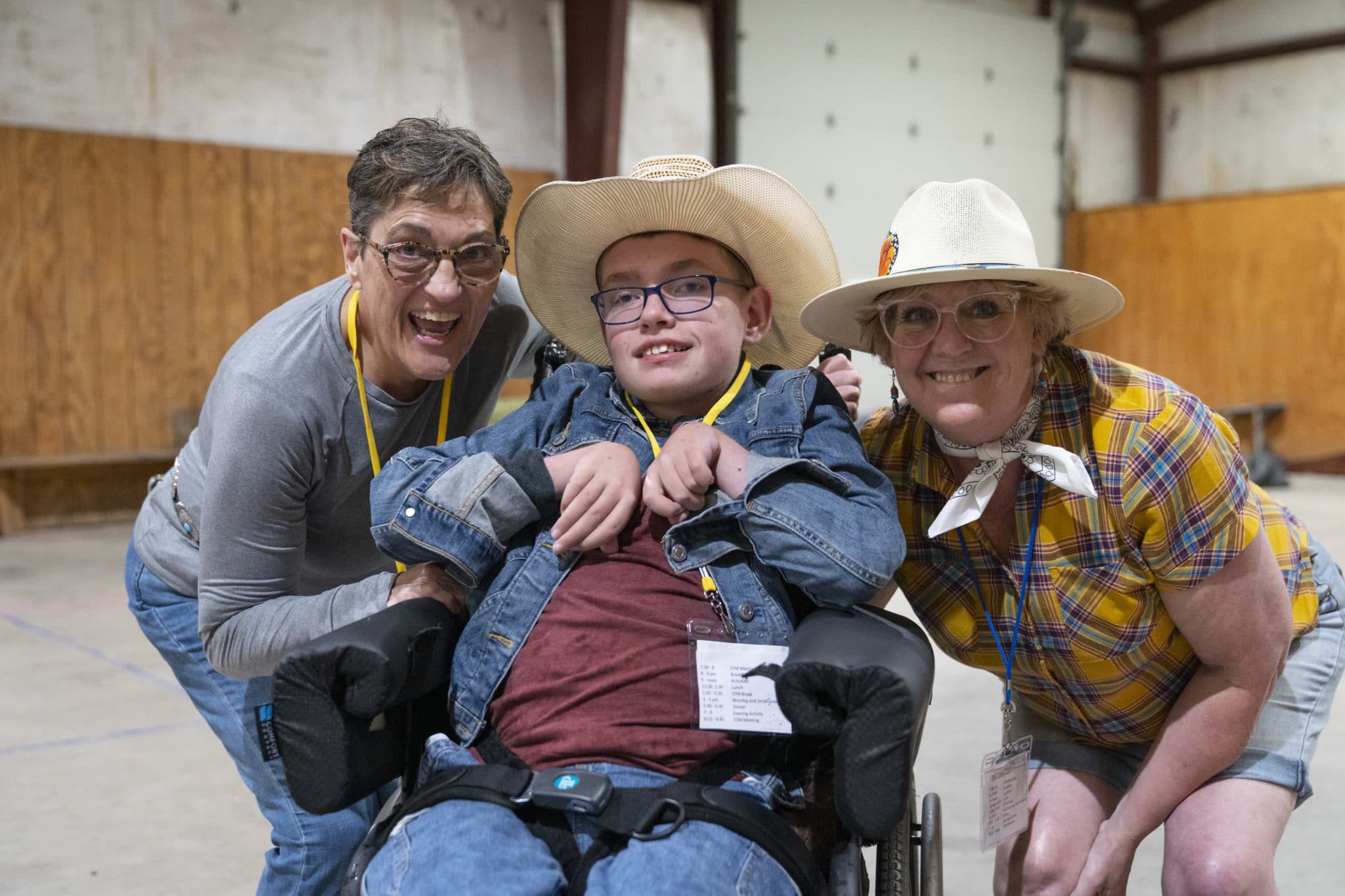Grandma Julie stands to the left of her grandson, Tyler who is a wheelchair user. To the right of Tyler is a Family Retreat Volunteer. All are smiling.