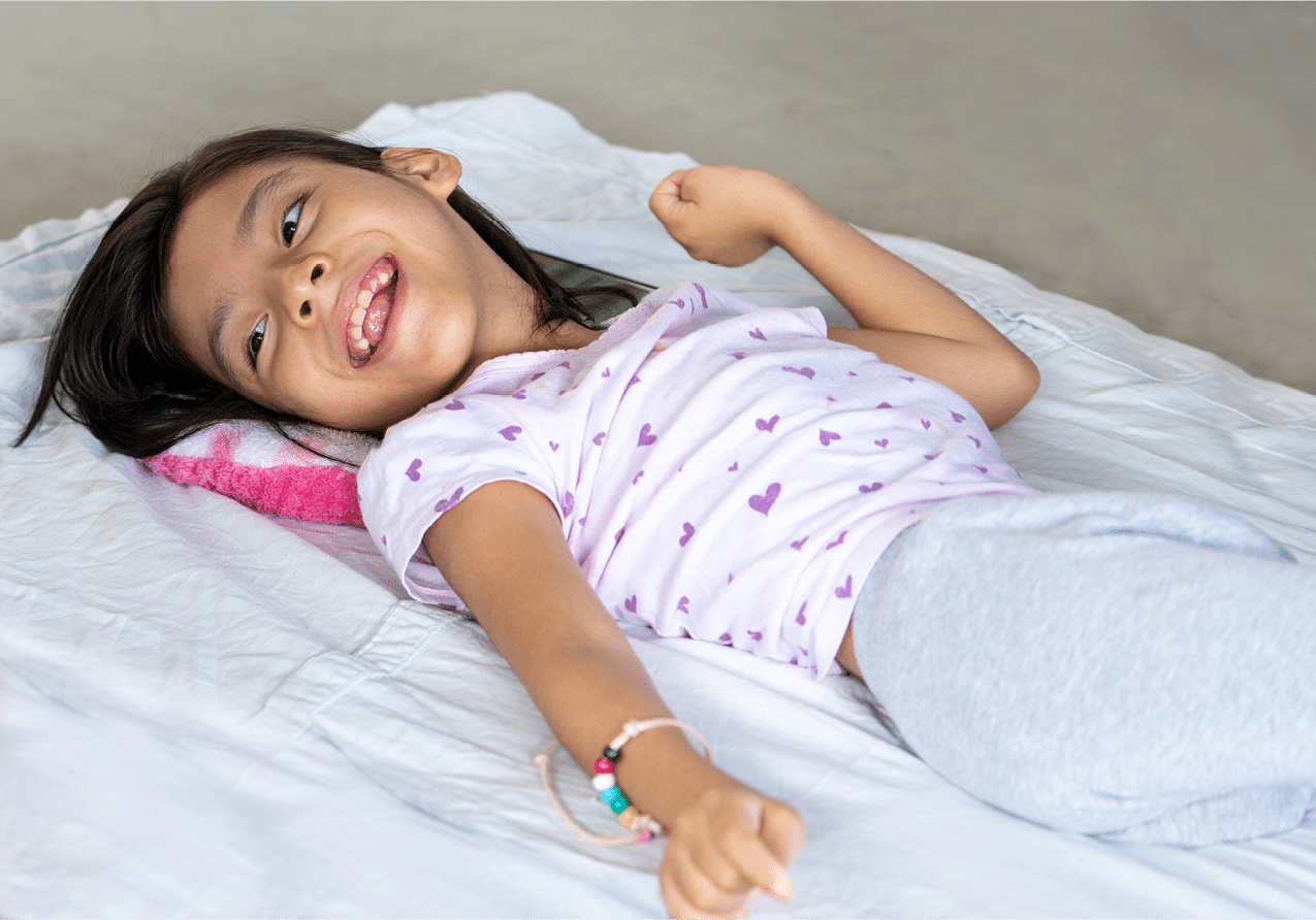 Victoria smiles as she lays on her back on a blanket on the ground with a small pillow under her head.