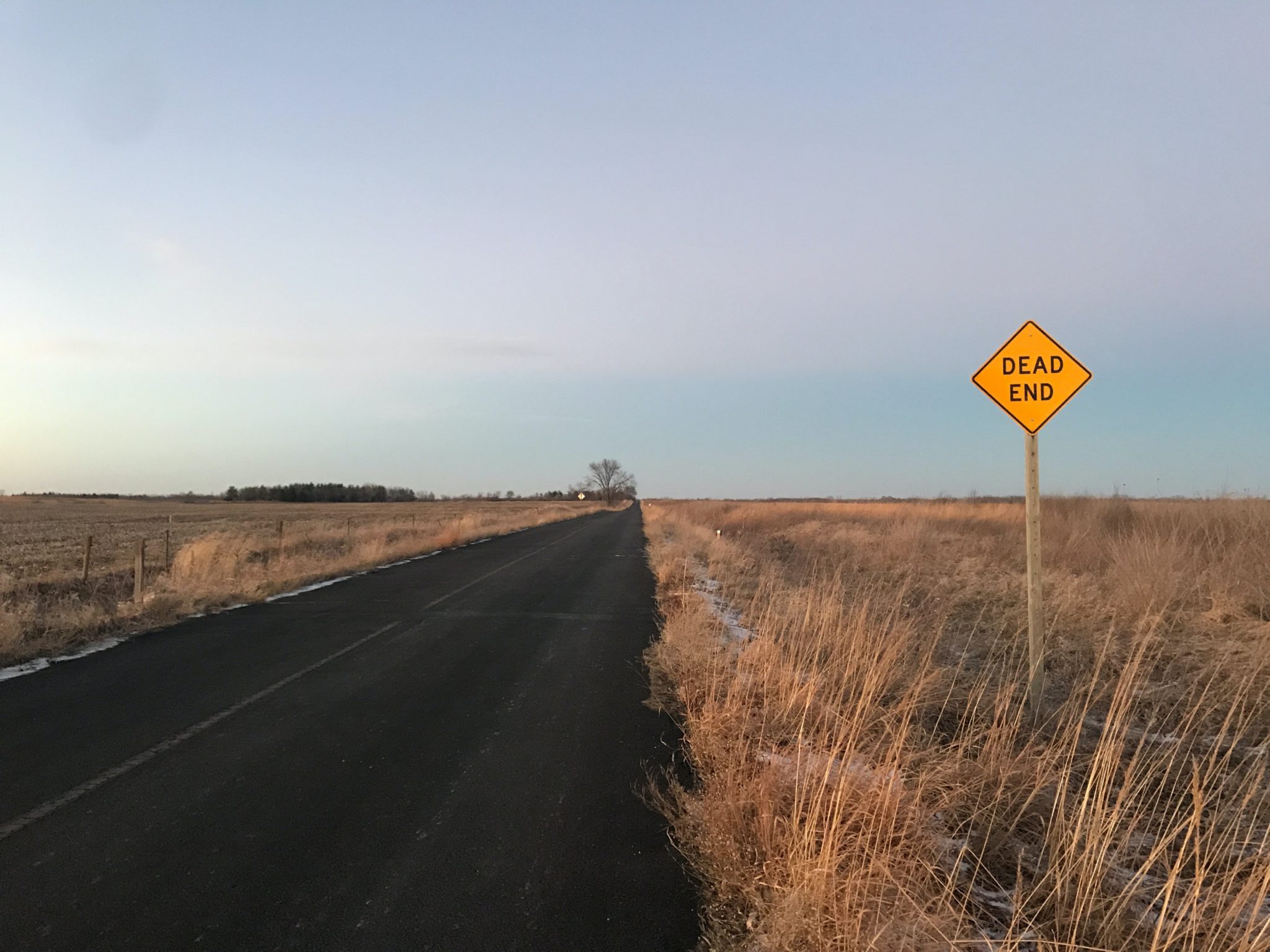 A paved road running through a field of dead grass, and a sign that says "Dead End" on the side.