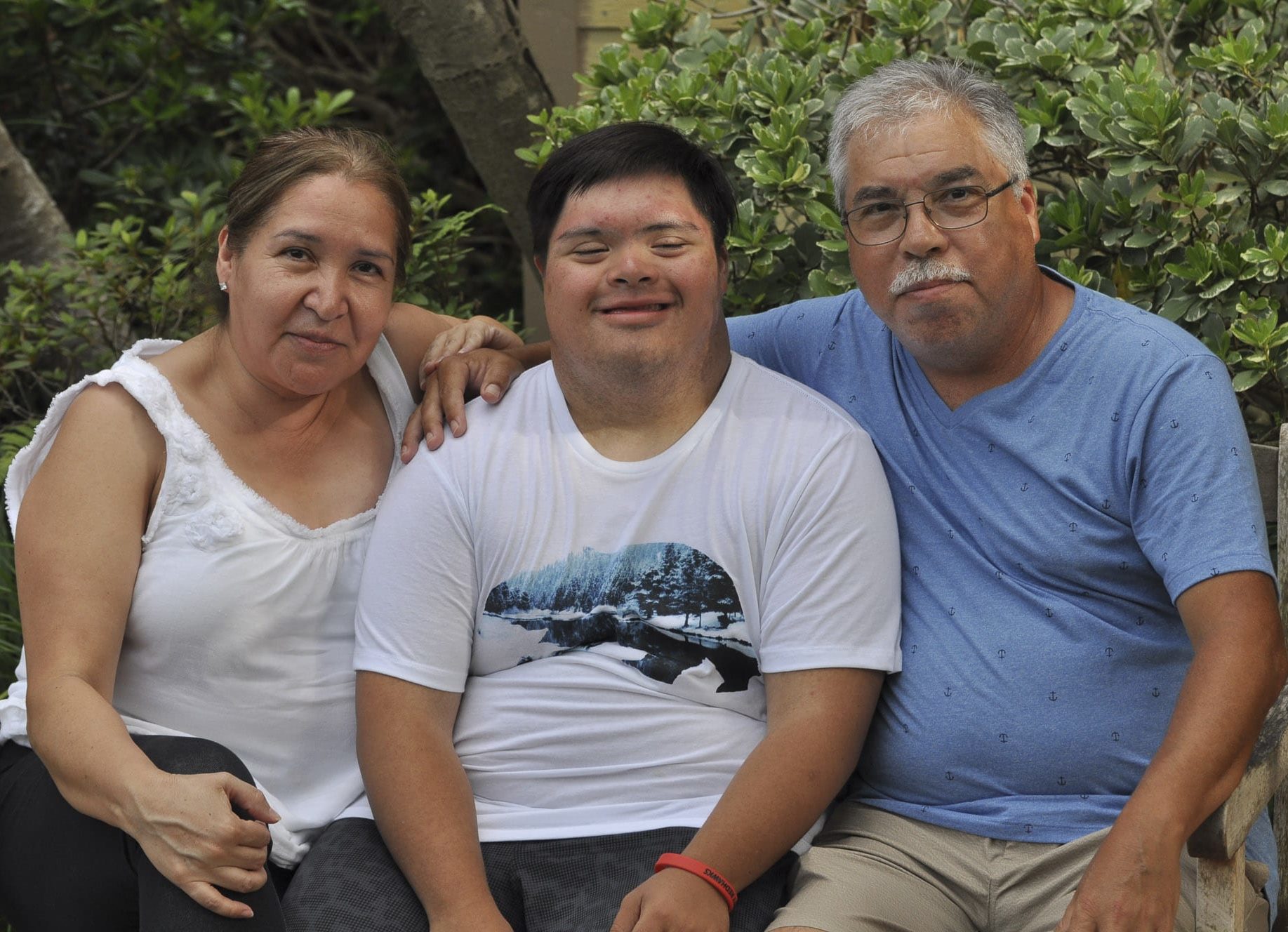 A mother and father siting on a bench with their son who has down syndrome in between them.