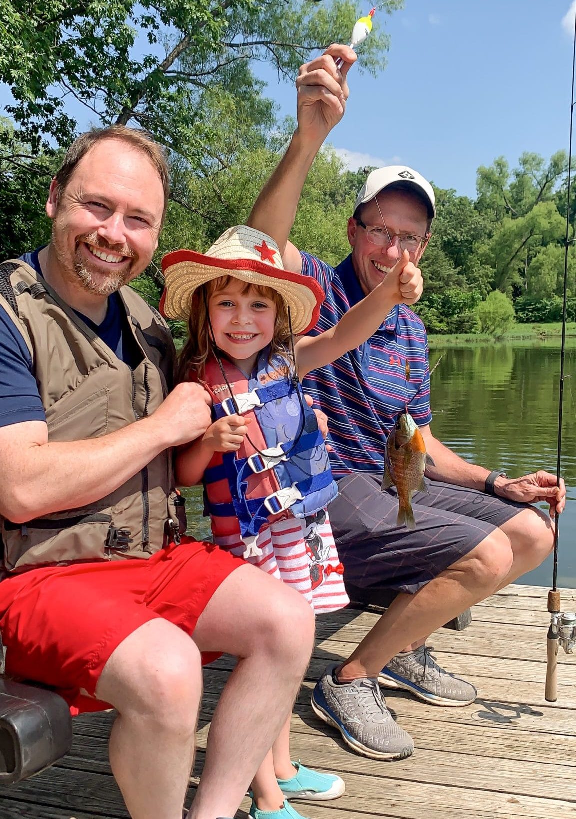 John (left), his daughter Matea (middle), and a Joni and Friends volunteer (right) smile for the camera while holding up the fish that Matea caught from the lake.