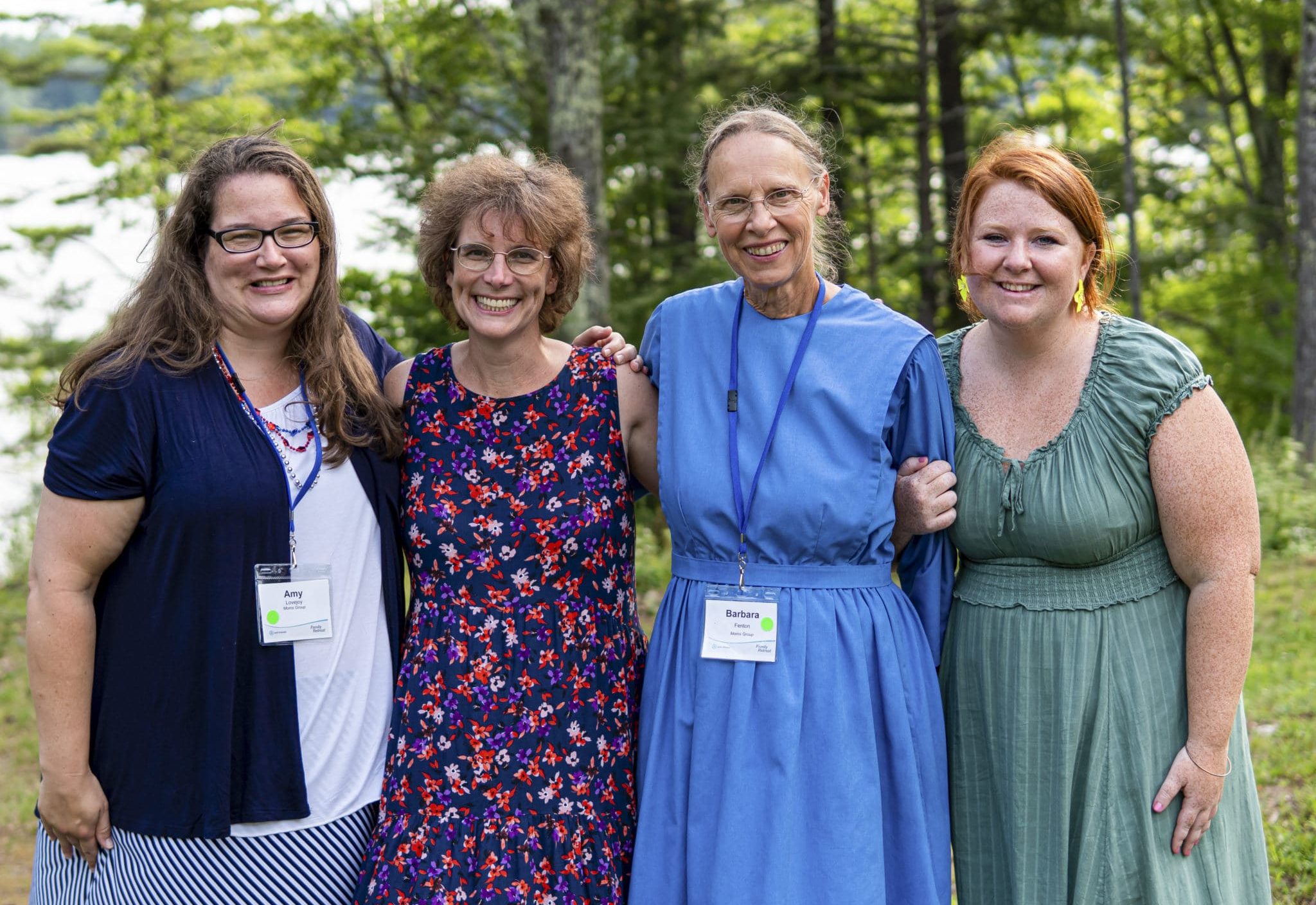 Jacqui with three other ladies from retreat, some moms of attendees and some volunteers. All are wearing dresses and smiling at the camera with a lush forest in the background.