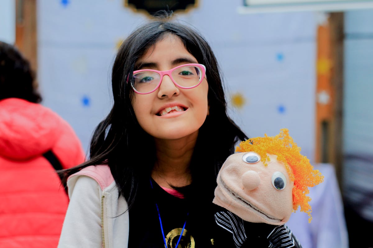 A close up of Priscilla smiling at the camera with her little reading glasses on and a puppet in her arms.