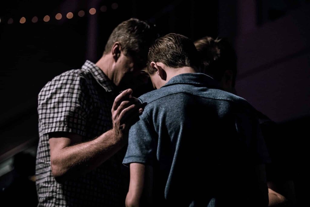 A group of three people praying together with their head's bowed together as they lay hands on one another.