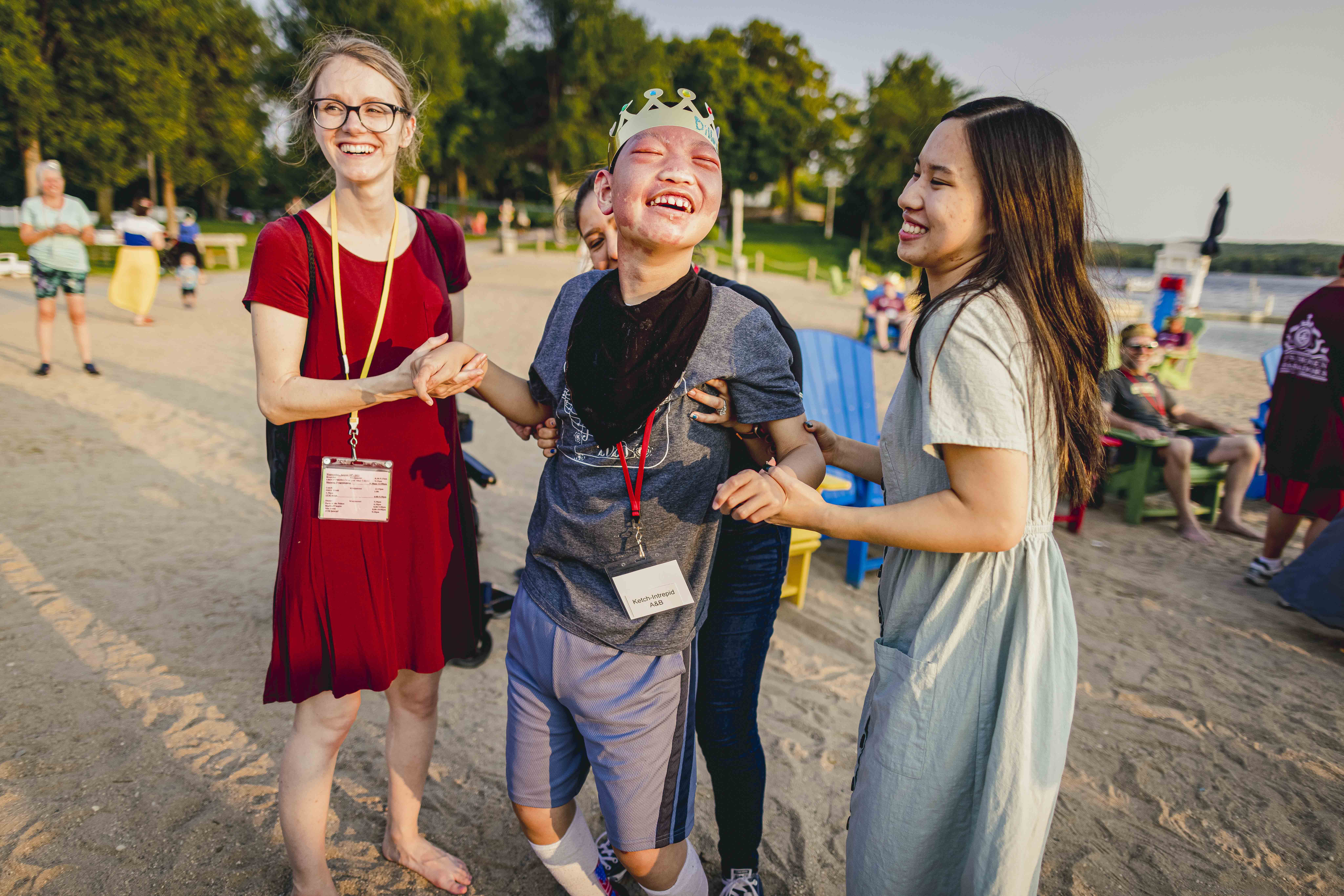 Dillion, his two sisters and his Joni and Friends Buddy smiling and laughing on the beach. Dillion is wearing a golden plastic crown.