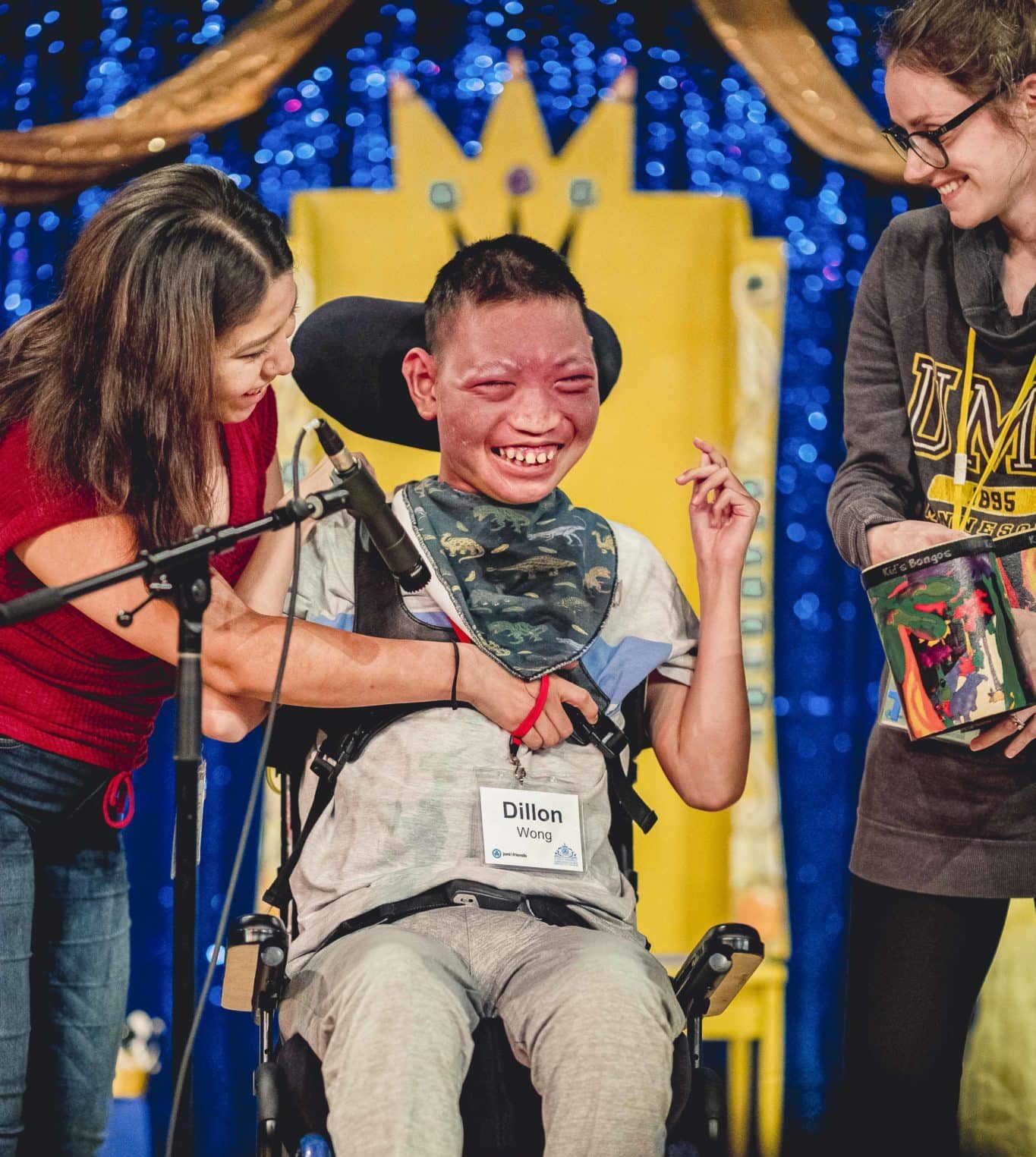 Dillion smiling and laughing as he is on stage for the talent show seated in his wheelchair.