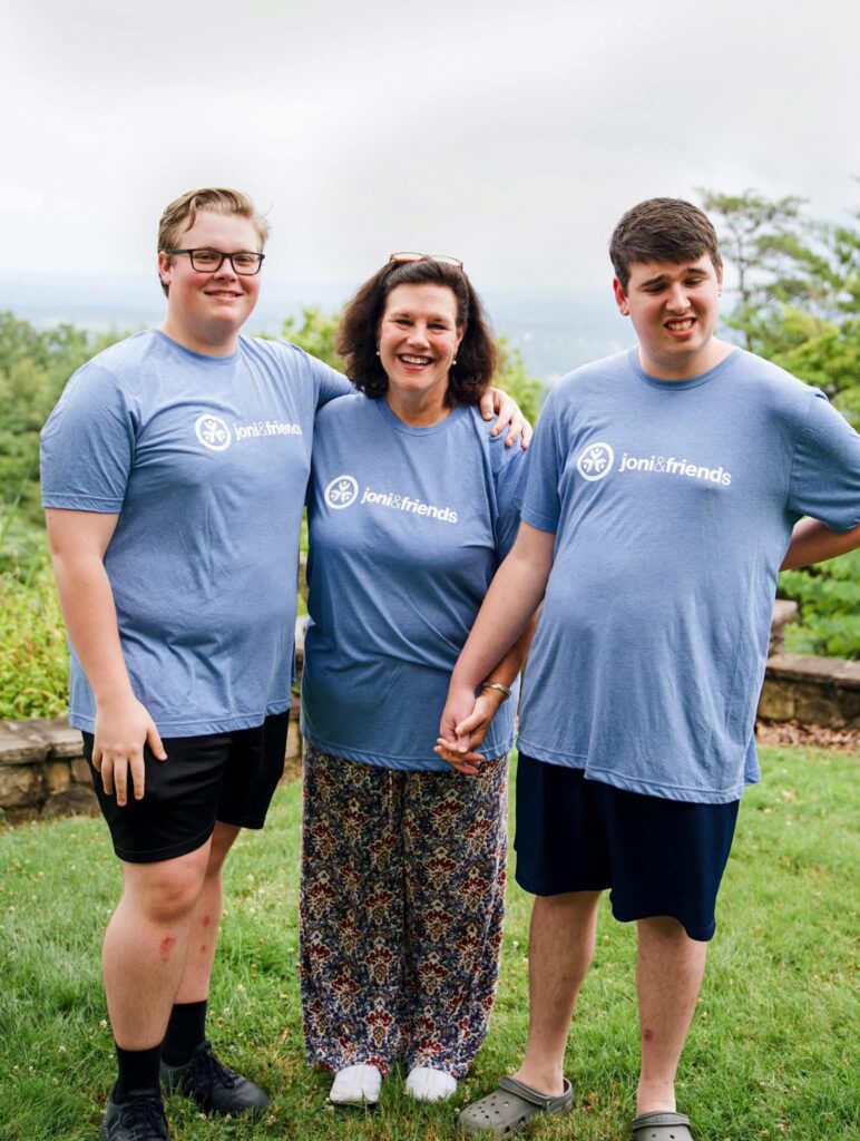 Family of 3 smiling and posing for picture wearing Joni and friends t-shirts.