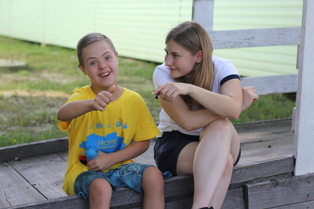A boy smiling and giving a thumbs up next to a volunteer at International Family Retreat