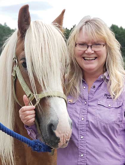Jodi standing next to her horse Solomon and smiling at the camera.