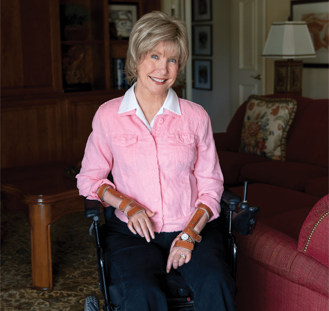 A portrait of Joni seated in her wheelchair in her living room smiling at the camera.
