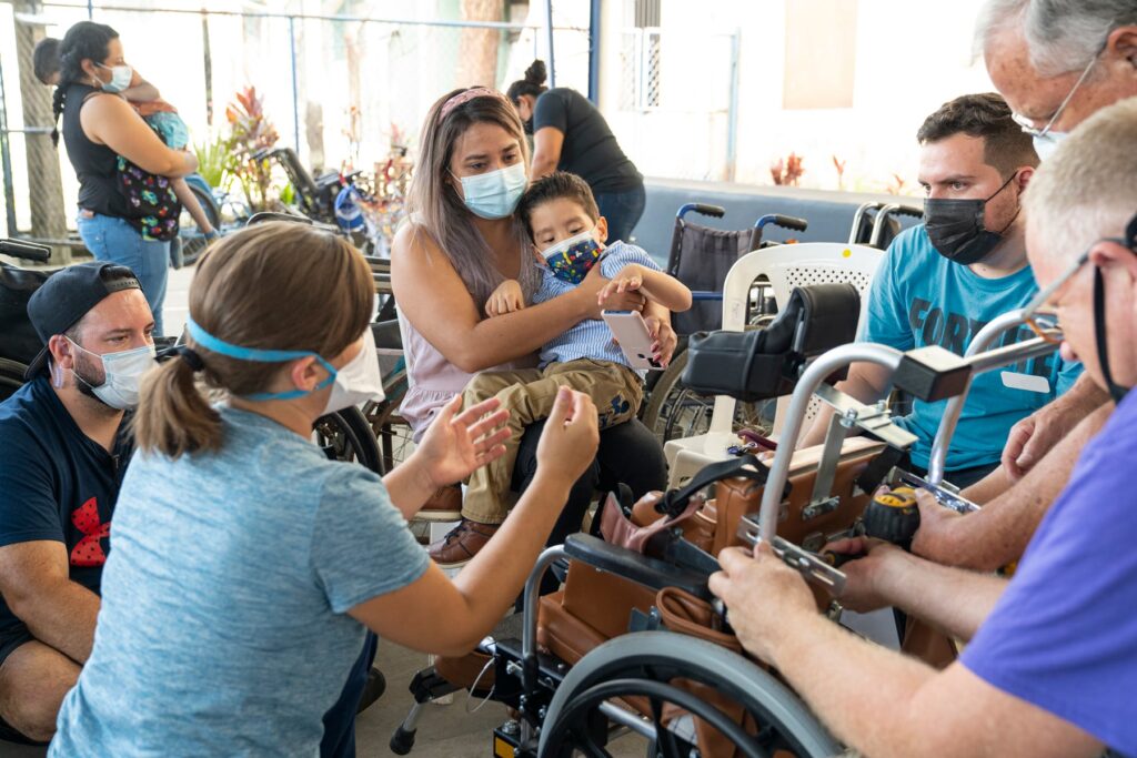 Ian's mother holding him as multiple Joni and Friends volunteers try to place him in his new wheelchair.