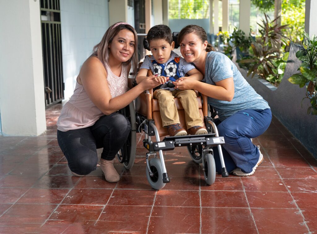 Ian seated in his wheelchair with his mom on his left and a Joni and Friends volunteer to his right.
