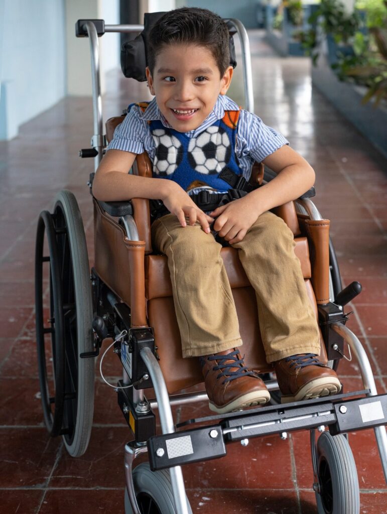 Little Ian smiling wide as he is seated in his brand new wheelchair.